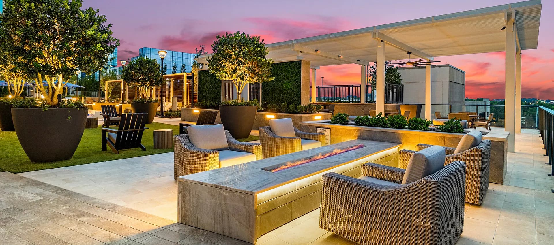 Luxurious rooftop lounge with modern wicker seating, ambient lighting, and lush greenery against a stunning sunset backdrop.