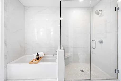 A white bathroom with a marble wall and a glass shower door.