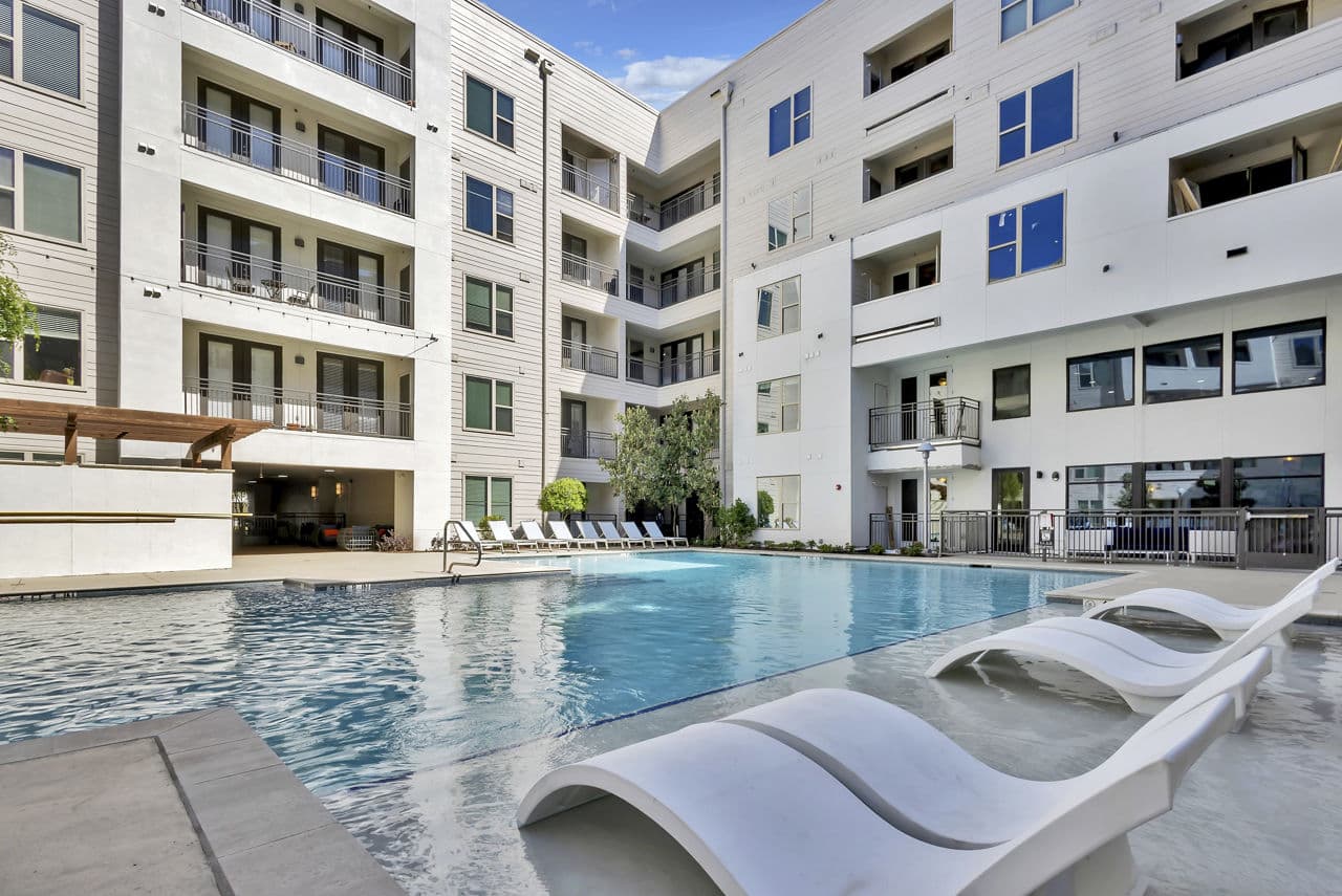 Luxurious outdoor pool at Oak & Ellum Apartments with modern lounge chairs and landscaped surroundings