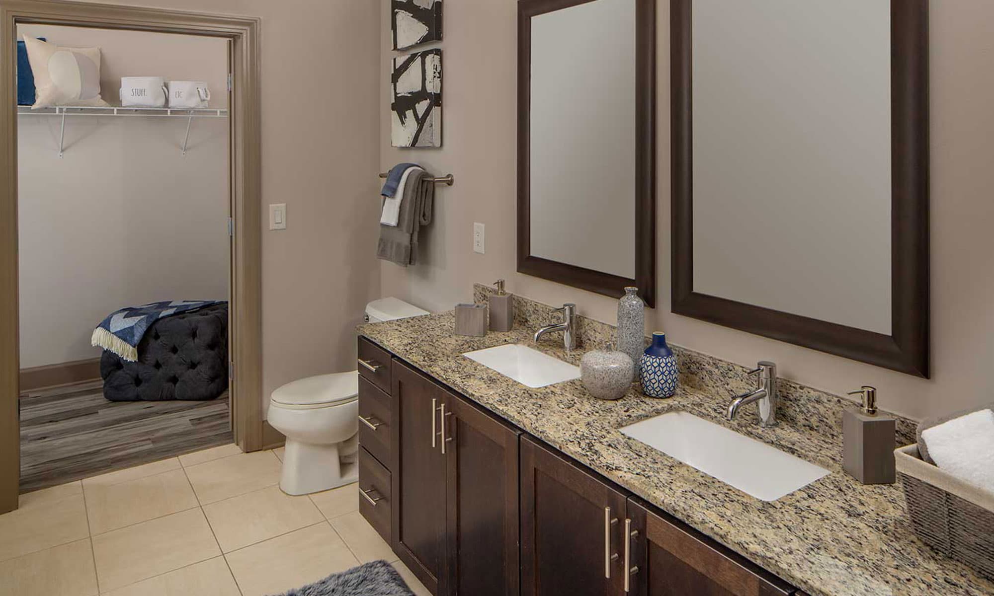 Bathroom with double sinks, granite counters, and walk-in closet