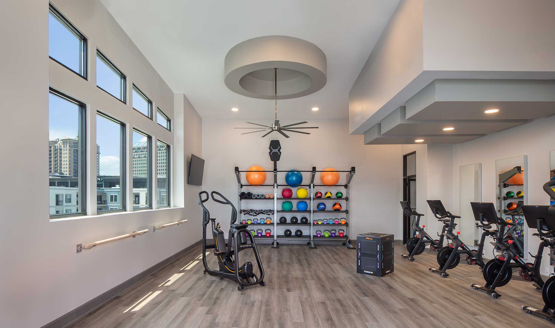 fitness center with stretching bars, large windows overlooking city, ceiling fan, bike machines, and various free weights