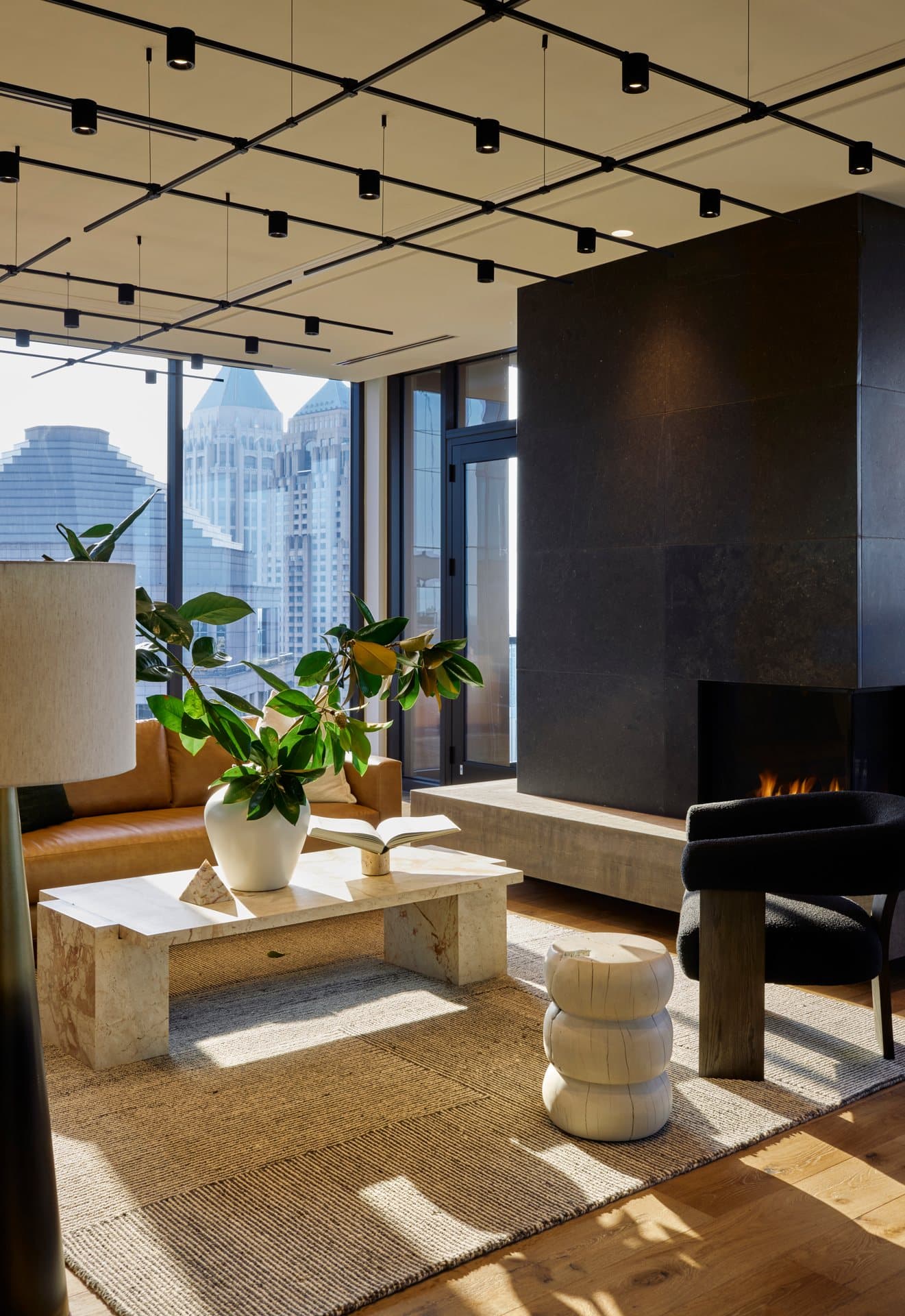 Stylish lounge area with seating, a coffee table, plants, and city skyline views through large windows.
