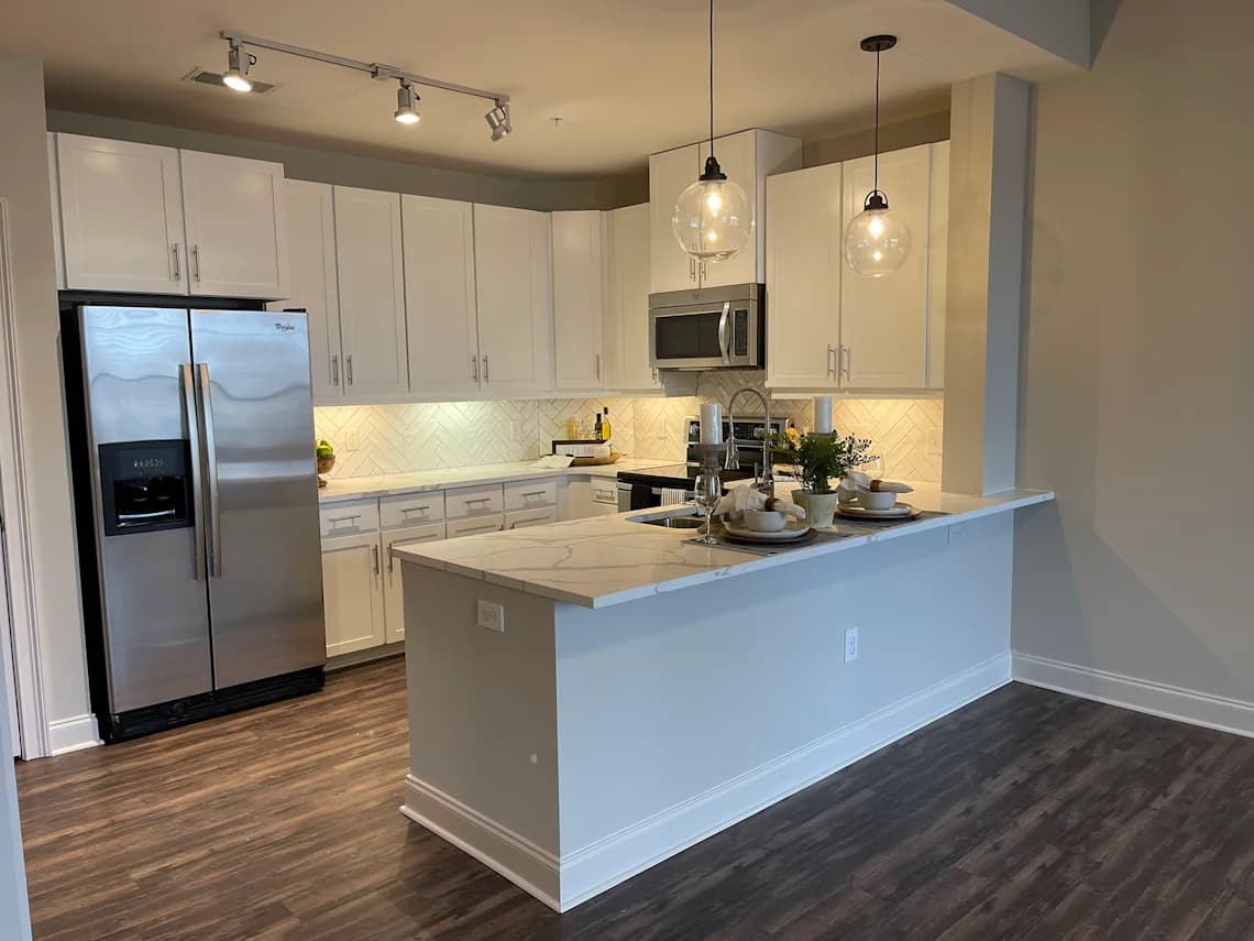 A kitchen with a refrigerator, microwave, and a counter with a bowl of fruit on it.